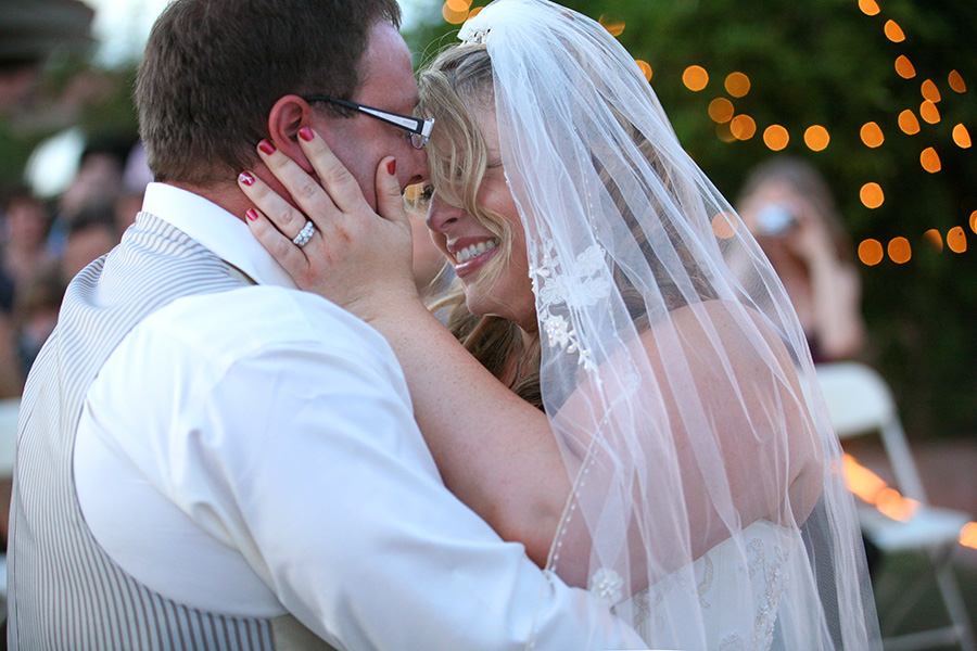 Bride and groom embracing beneath string lights