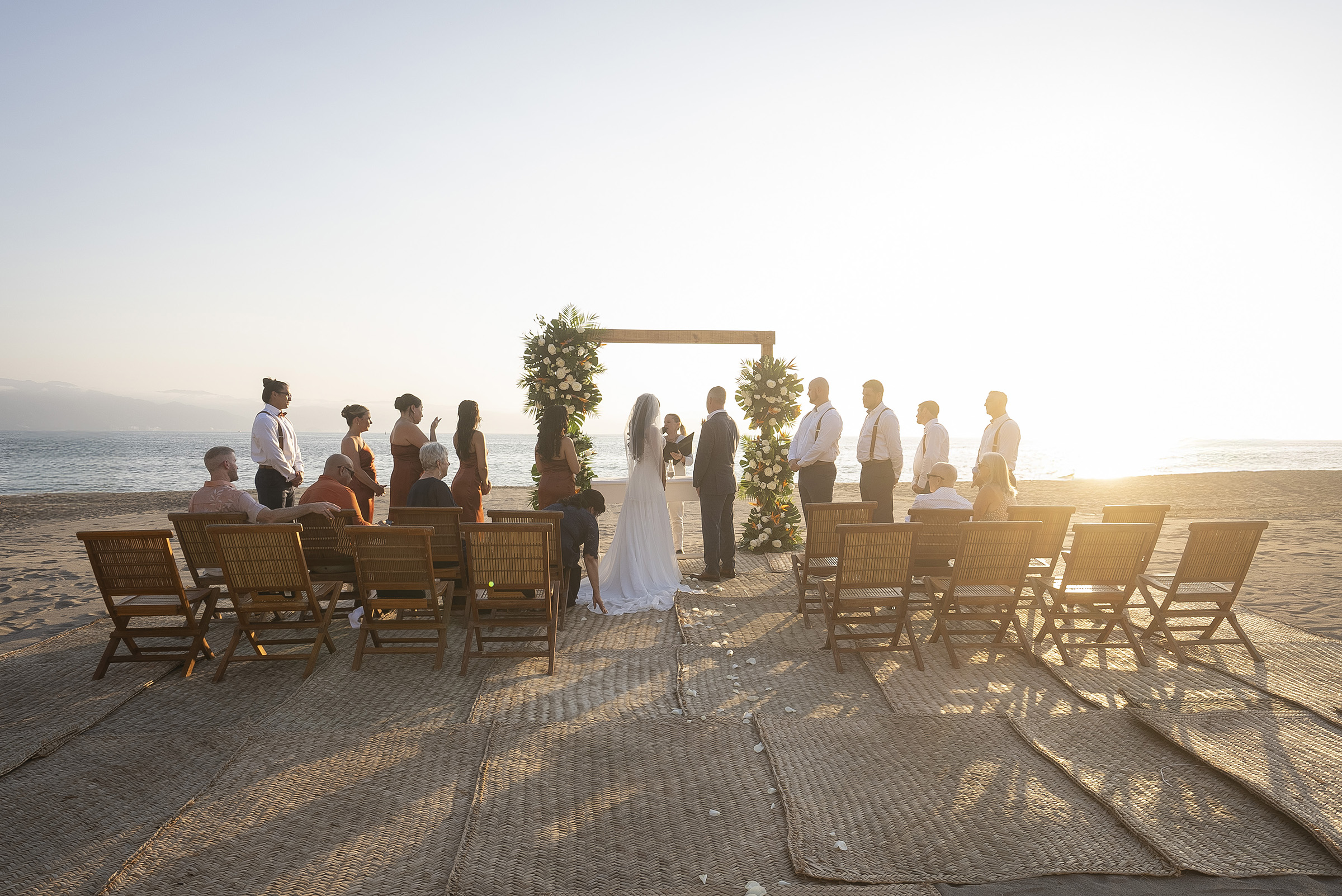Beach wedding ceremony beneath a floral arch at sunset