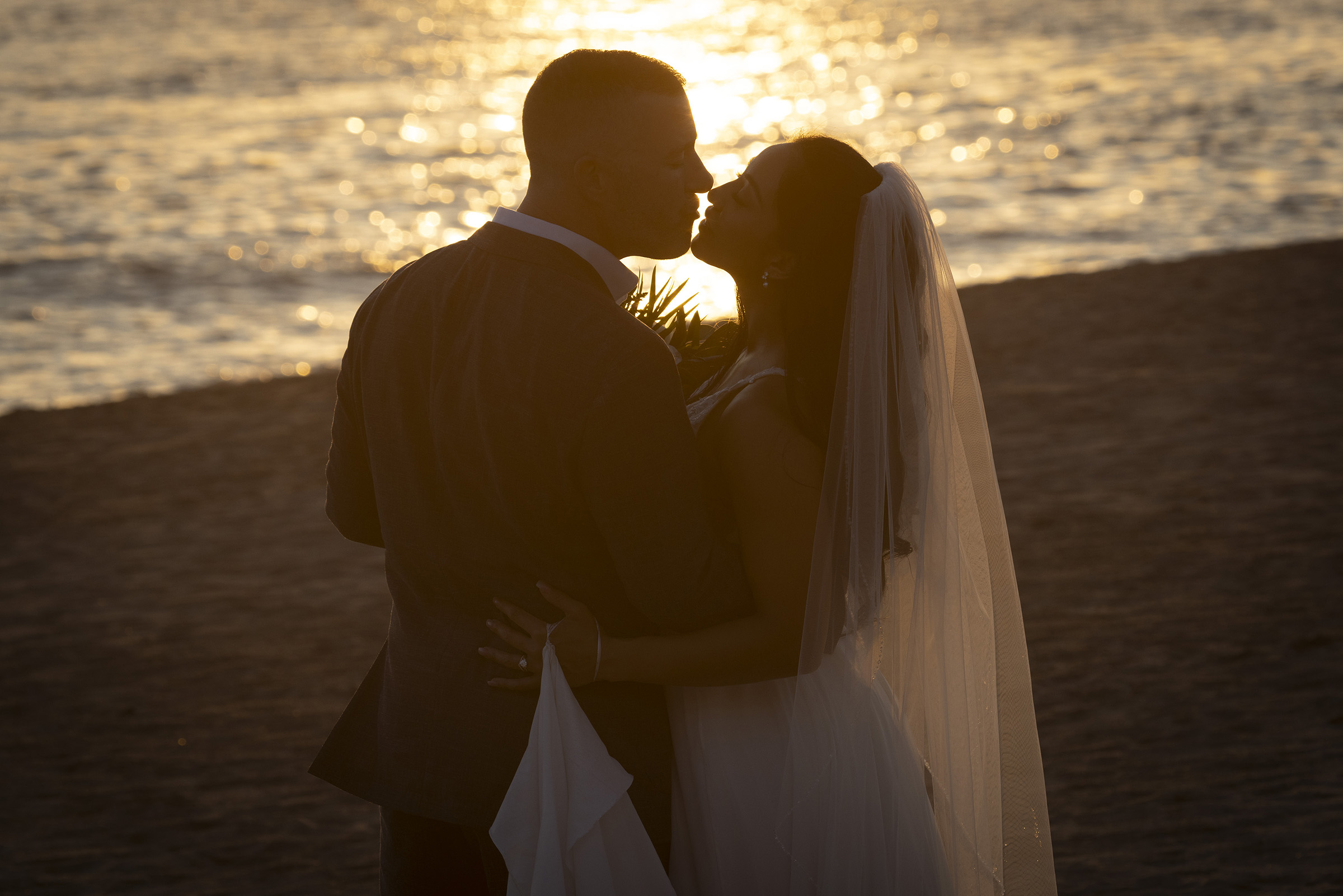 Wedding couple kissing beside the water at sunset